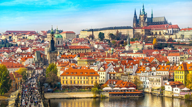 Panoramablick über die belebte Karlsbrücke auf die Prager Altstadt und die majestätische Prager Burg unter blauem Himmel