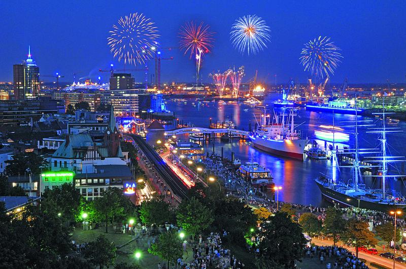 Silvesterfeuerwerk über dem blau beleuchteten Hamburger Hafen mit Schiffen bei Nacht